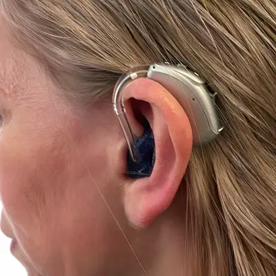 Beige NHS behind-the-ear hearing aid worn on an older man&rsquo;s ear